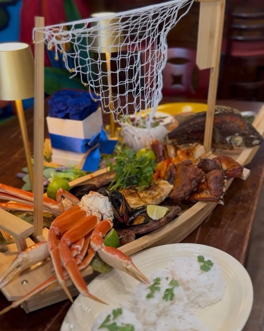 The Barco Fondeado, a wooden boat platter with crab legs, mussels, ribs, chicken and fried fish, next to a plate of rice.
