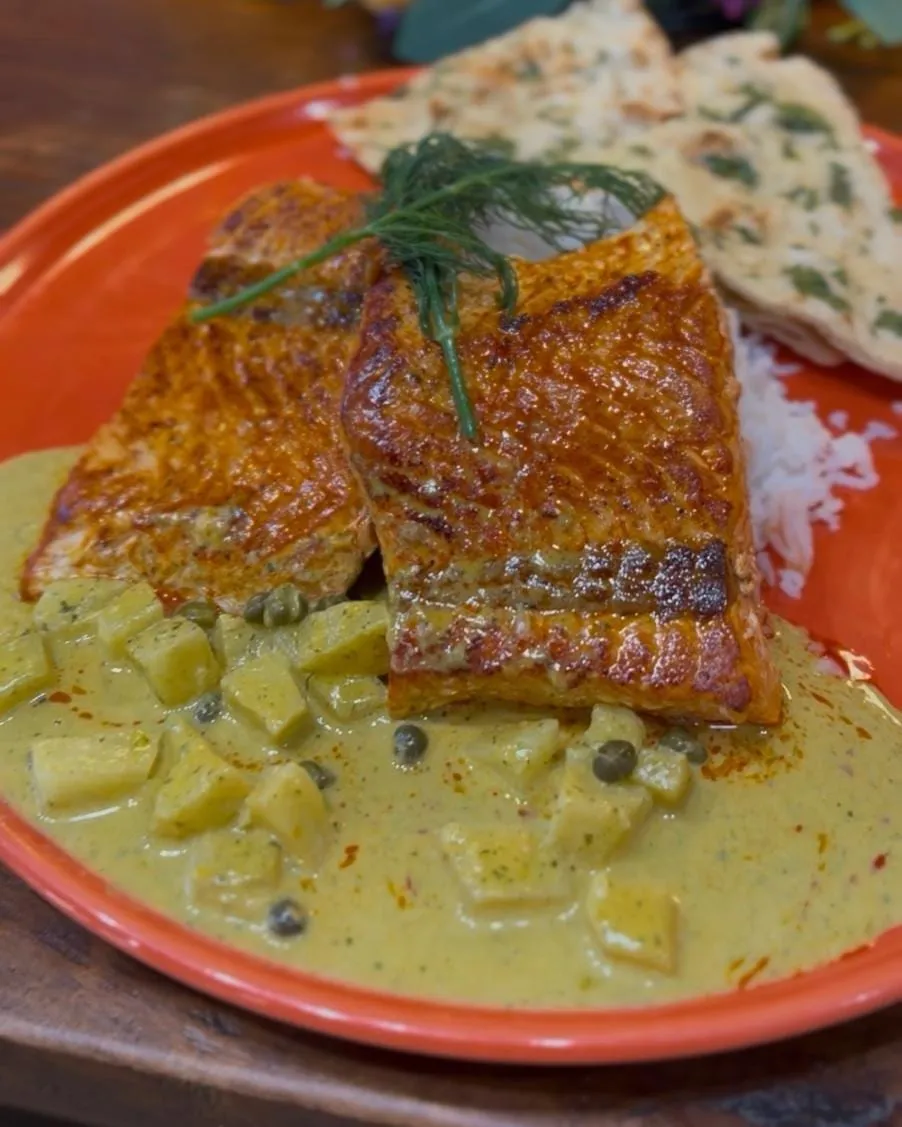 Two seared salmon fillets in a creamy cilantro sauce with pineapple, with basmati rice and naan.