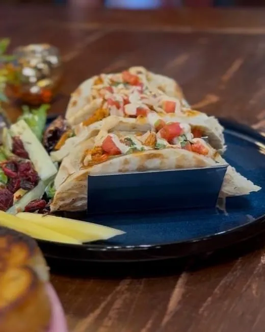 Salmon tacos in toasted naan topped with pico de gallo and crema, with mango slices and salad.