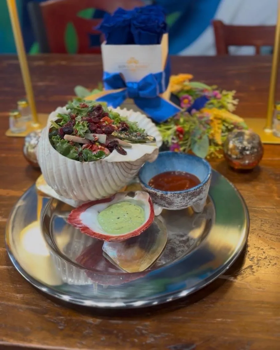Greens with dried cranberries and cucumber served in a large seashell, with two dipping sauces.